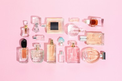 Photo of Bottles of various perfumes on pink background, flat lay