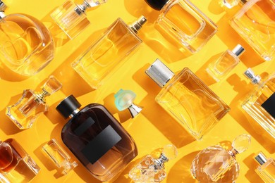 Photo of Bottles of various perfumes on yellow background, flat lay