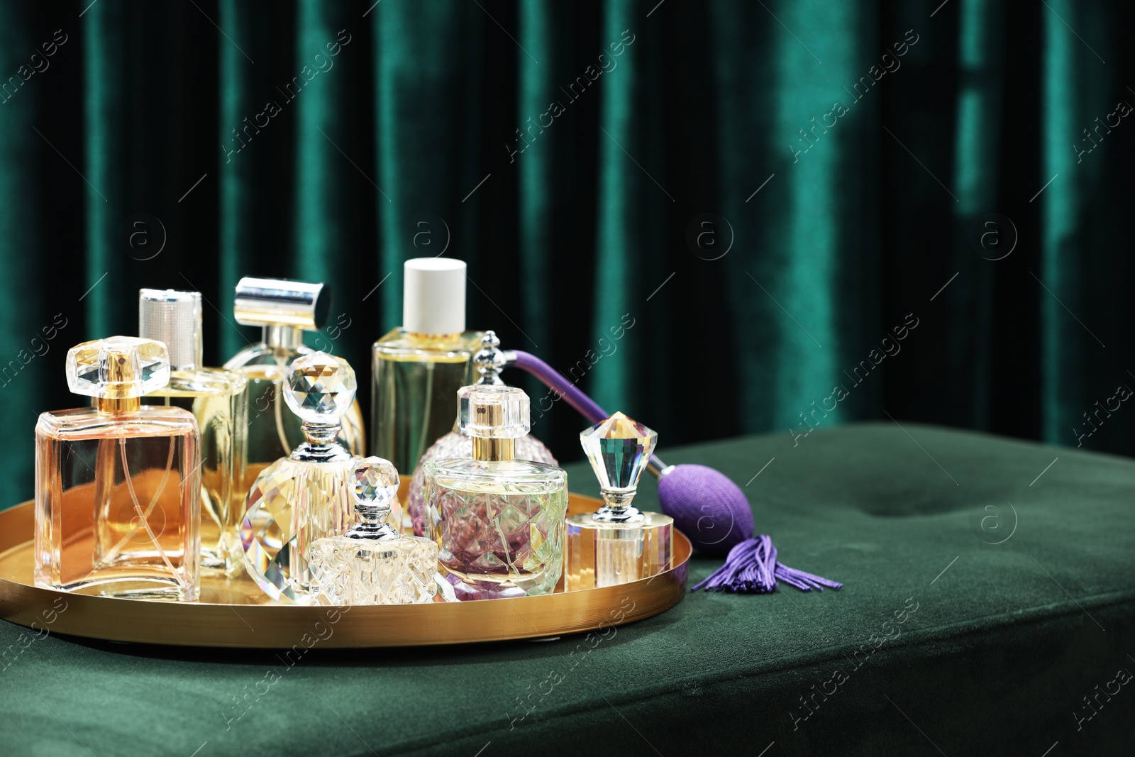 Different luxury perfumes on green pouf near teal curtains, space for text Photo of Different luxury perfumes on green pouf near teal curtains, space for text