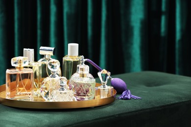 Photo of Different luxury perfumes on green pouf near teal curtains, space for text