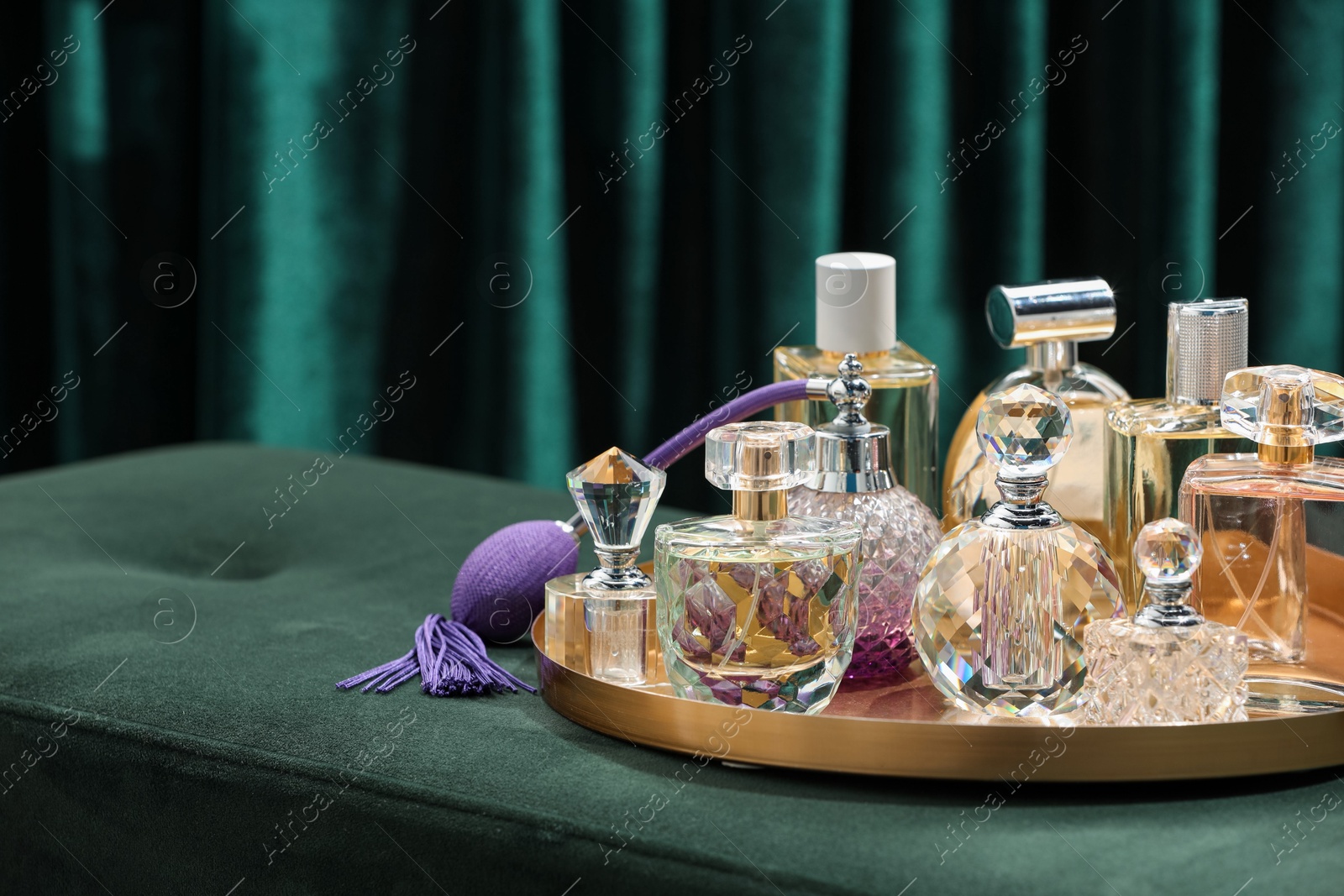 Different luxury perfumes on green pouf near teal curtains, closeup. Space for text Photo of Different luxury perfumes on green pouf near teal curtains, closeup. Space for text