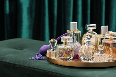 Photo of Different luxury perfumes on green pouf near teal curtains, closeup. Space for text