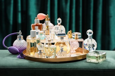 Photo of Different luxury perfumes on green pouf near teal curtains