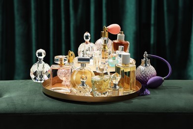 Photo of Different luxury perfumes on green pouf near teal curtains