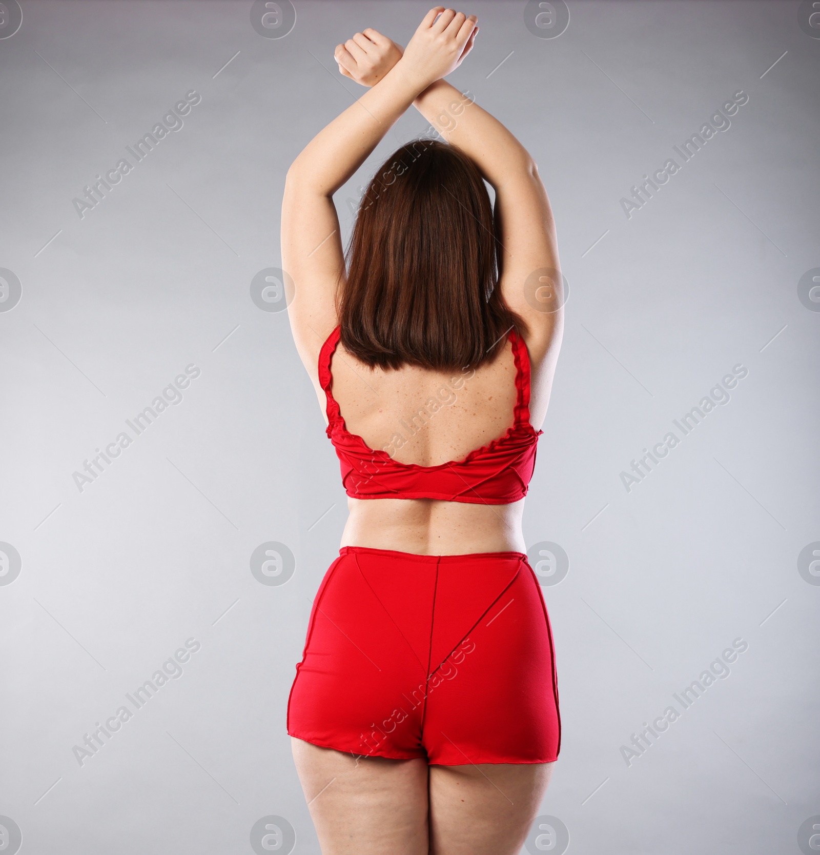 Photo of Woman in red underwear on light grey background, back view. Cellulite problem