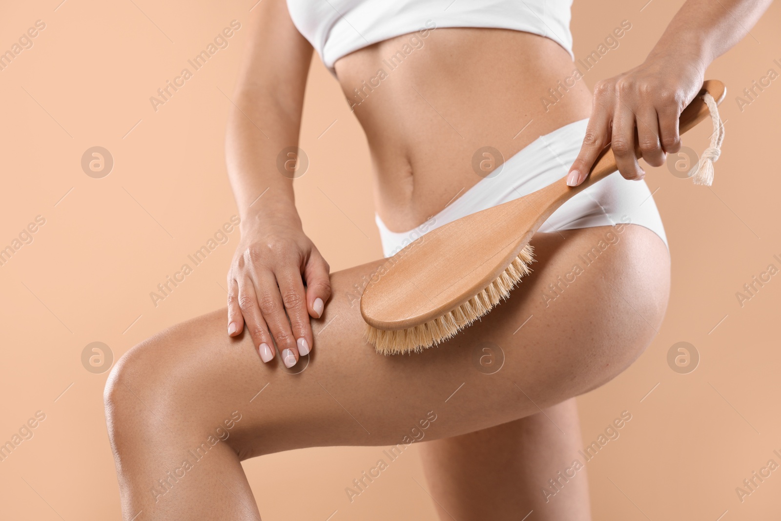 Photo of Woman doing anti cellulite massage with brush on beige background, closeup