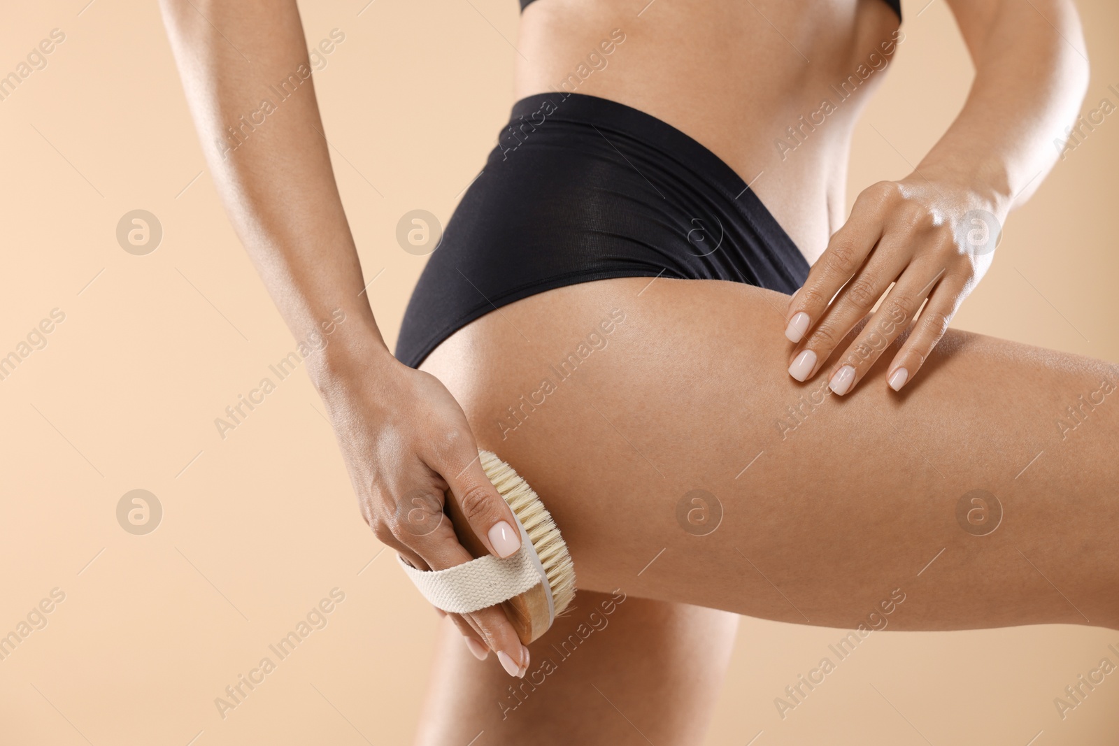 Photo of Woman doing anti cellulite massage with brush on beige background, closeup