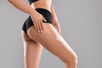 Woman applying anti cellulite cream on grey background, closeup