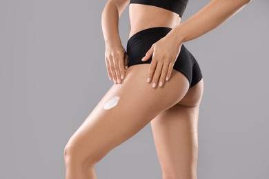 Photo of Woman applying anti cellulite cream on grey background, closeup