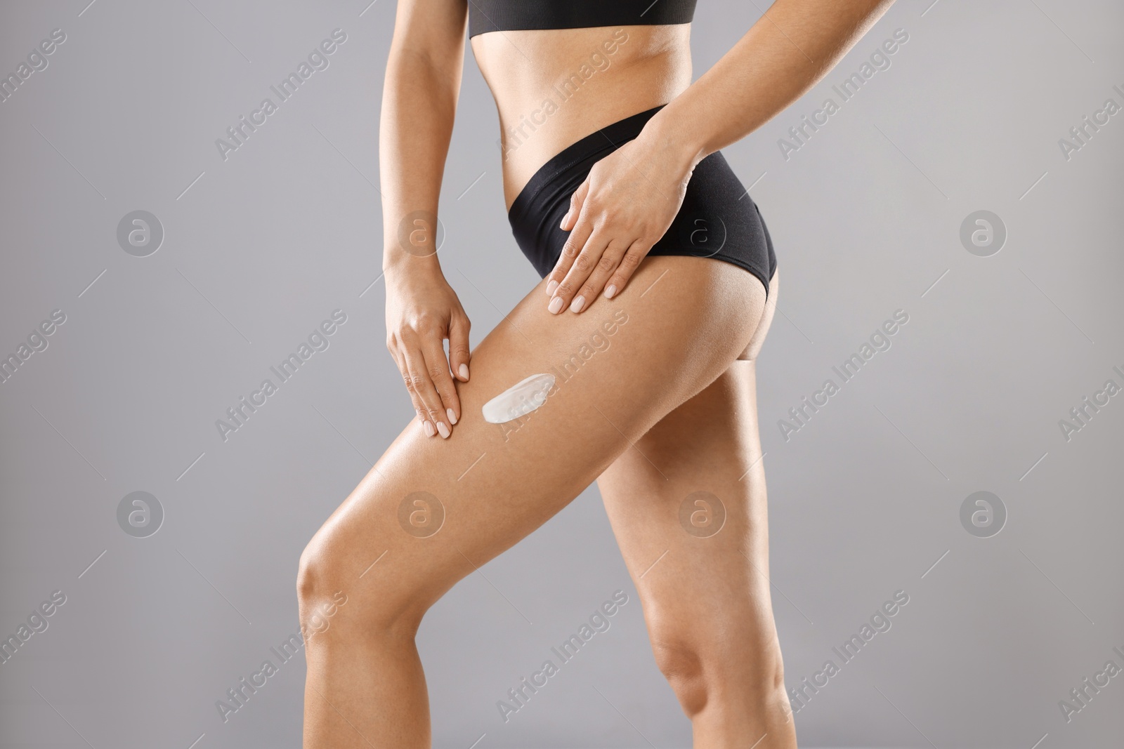 Photo of Woman applying anti cellulite cream on grey background, closeup