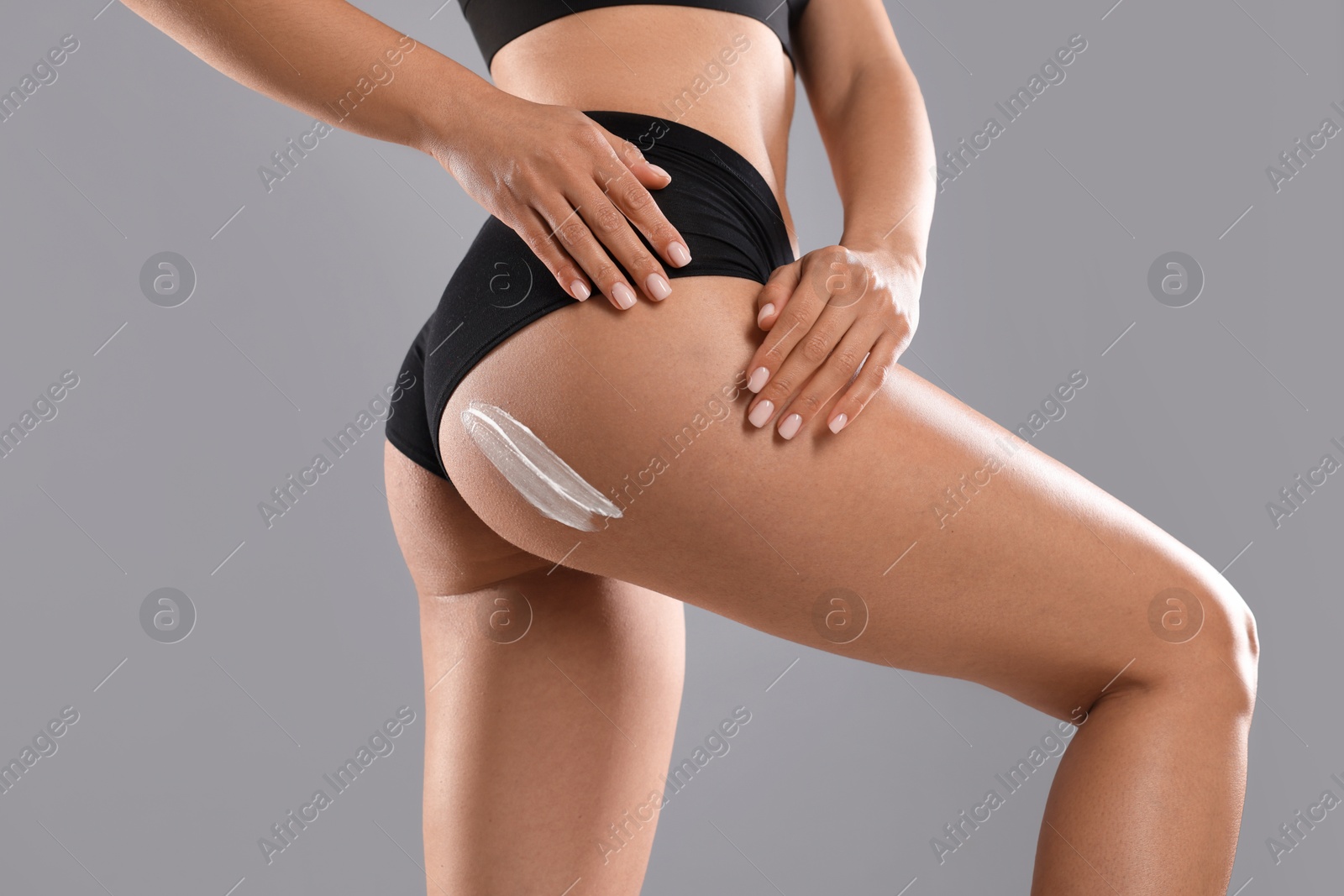 Photo of Woman applying anti cellulite cream on grey background, closeup