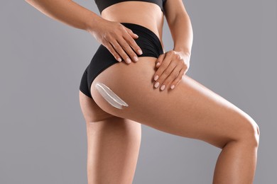 Woman applying anti cellulite cream on grey background, closeup