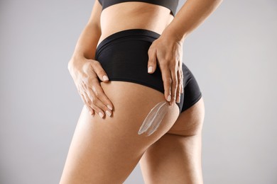 Photo of Woman applying anti cellulite cream on grey background, closeup