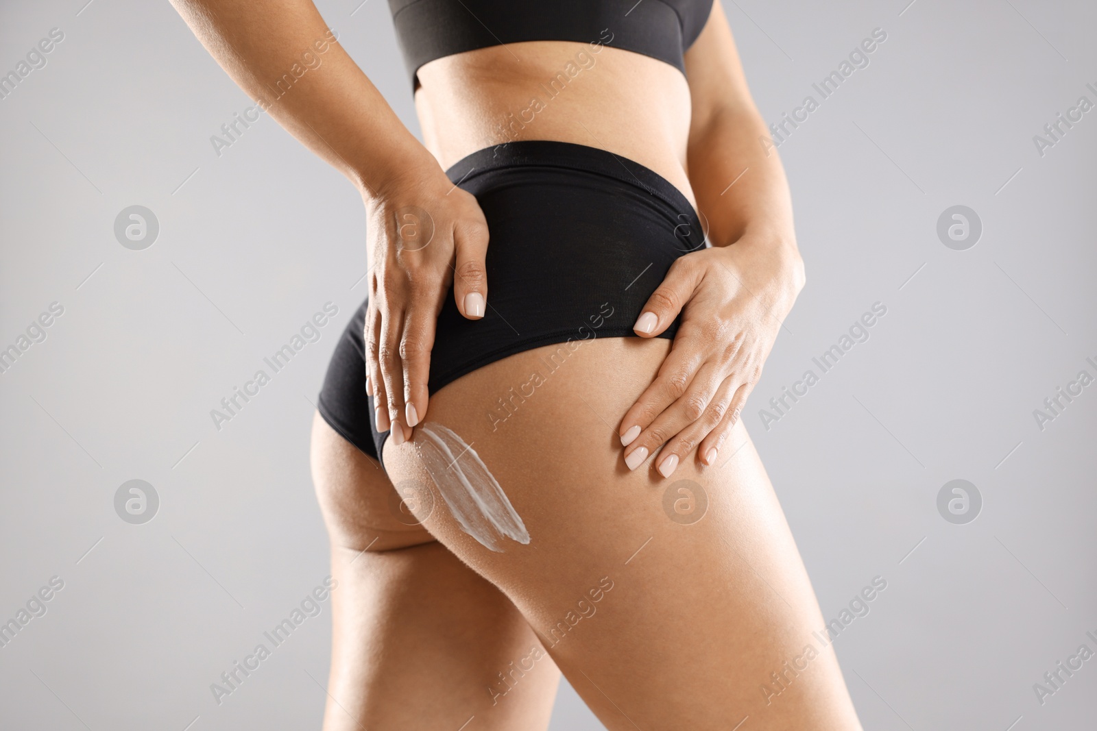 Photo of Woman applying anti cellulite cream on grey background, closeup