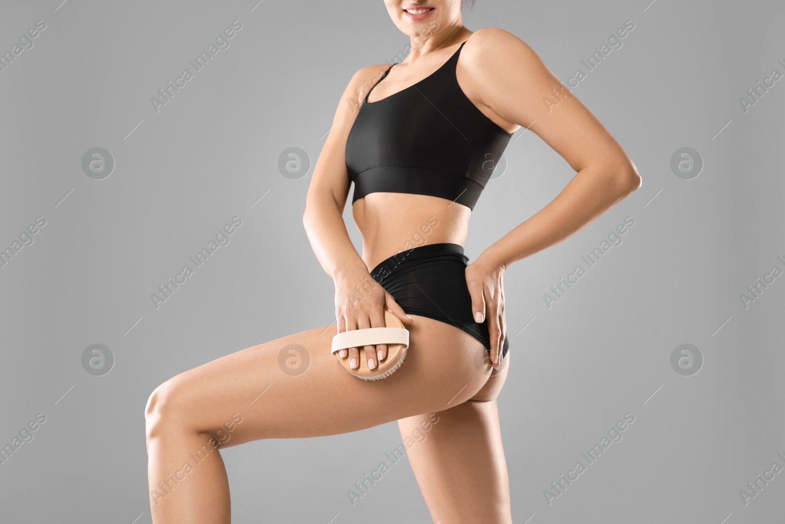 Photo of Woman doing anti cellulite massage with brush on grey background, closeup