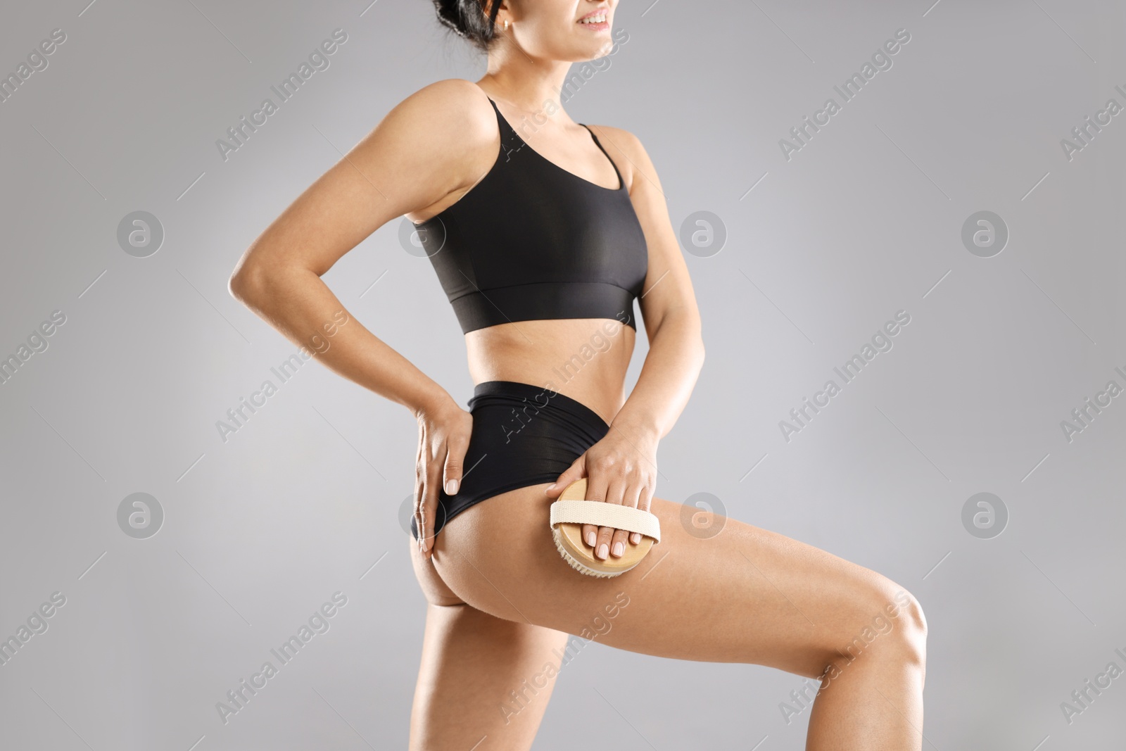 Photo of Woman doing anti cellulite massage with brush on grey background, closeup