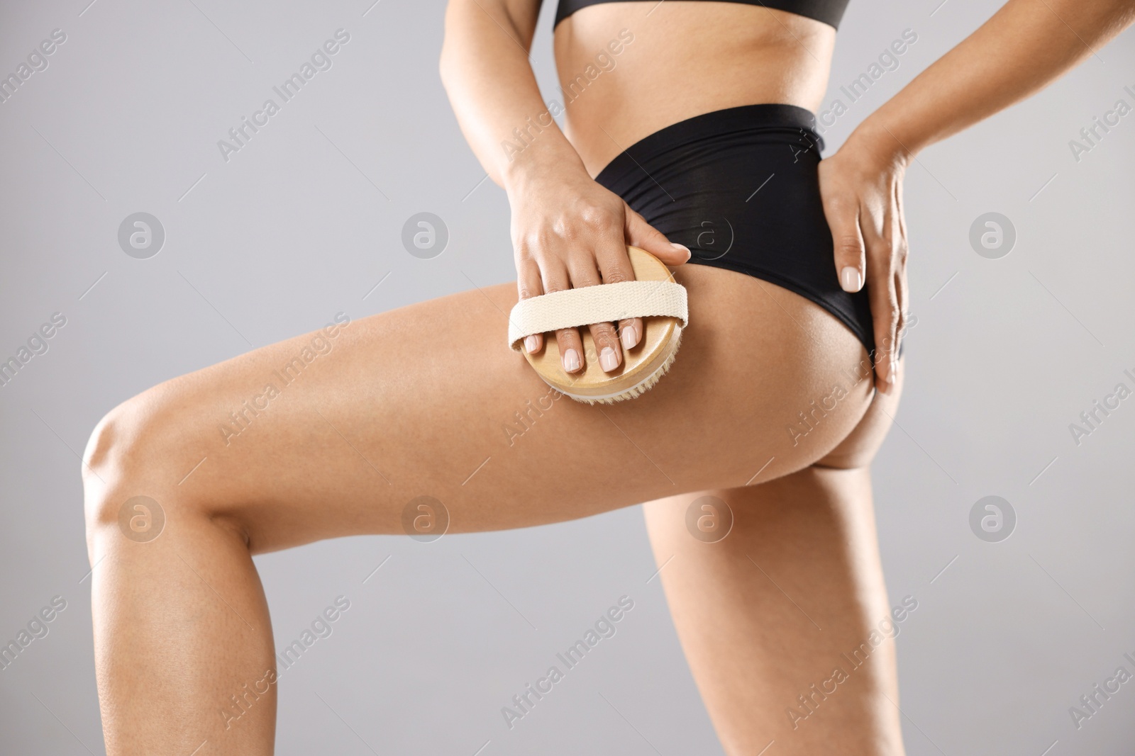 Photo of Woman doing anti cellulite massage with brush on grey background, closeup