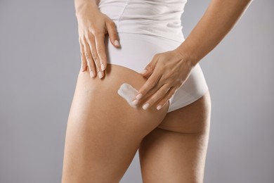 Photo of Woman applying anti cellulite cream on grey background, closeup