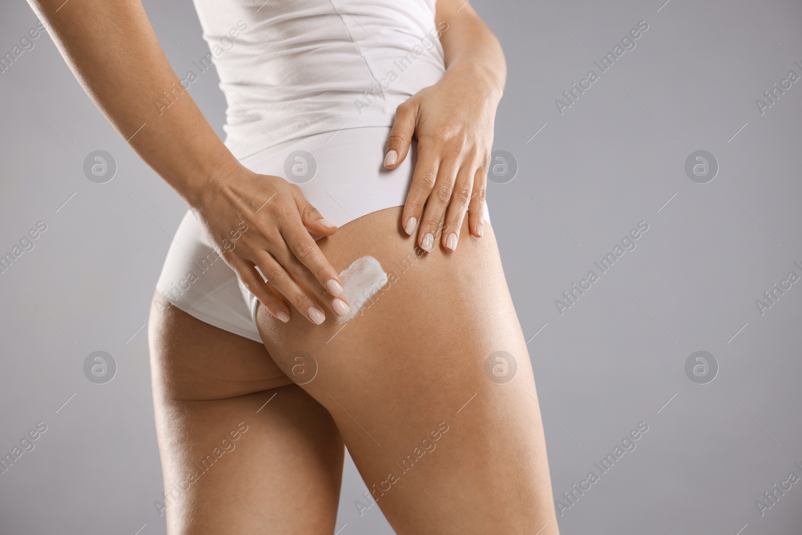 Photo of Woman applying anti cellulite cream on grey background, closeup