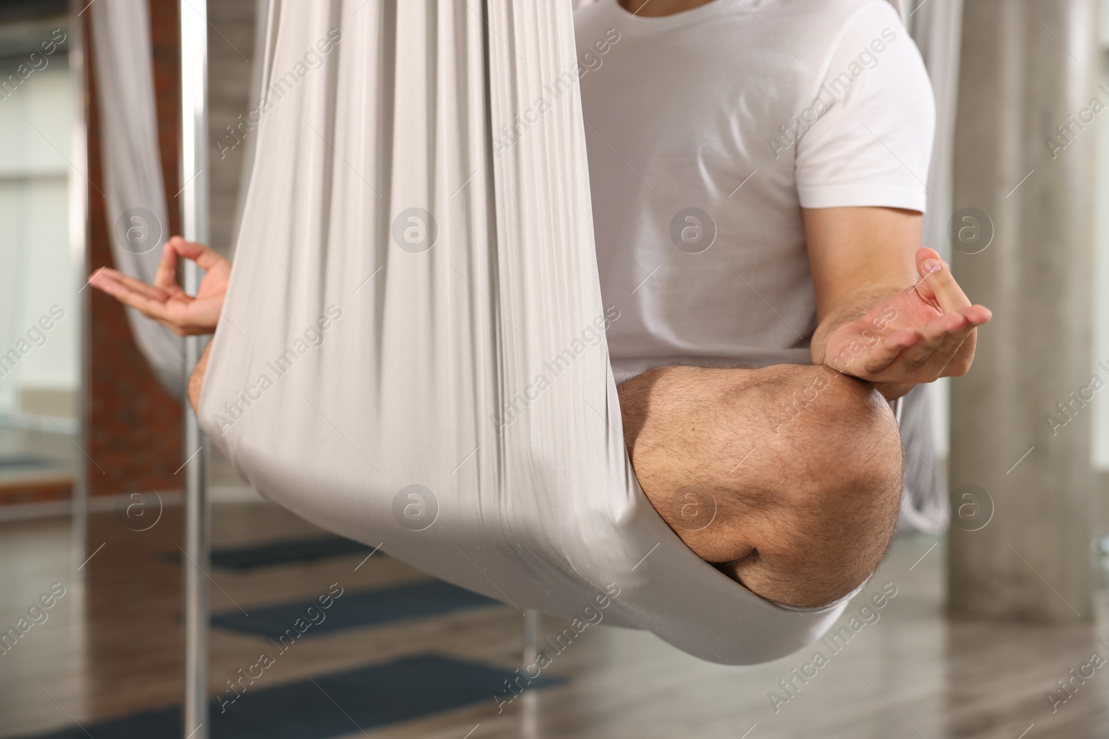 Photo of Man meditating in fly yoga hammock indoors, closeup