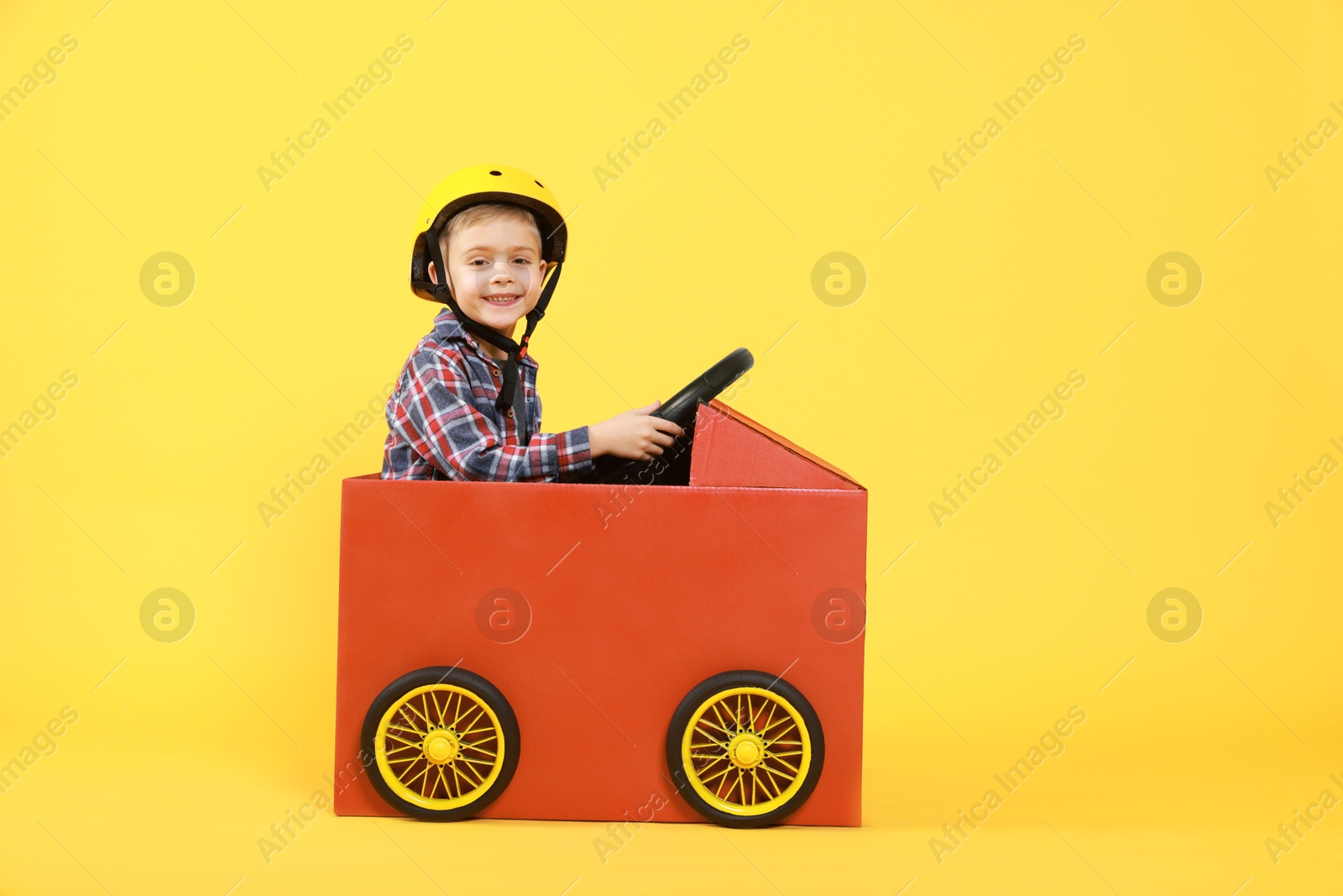 Photo of Little boy driving car made of cardboard on yellow background