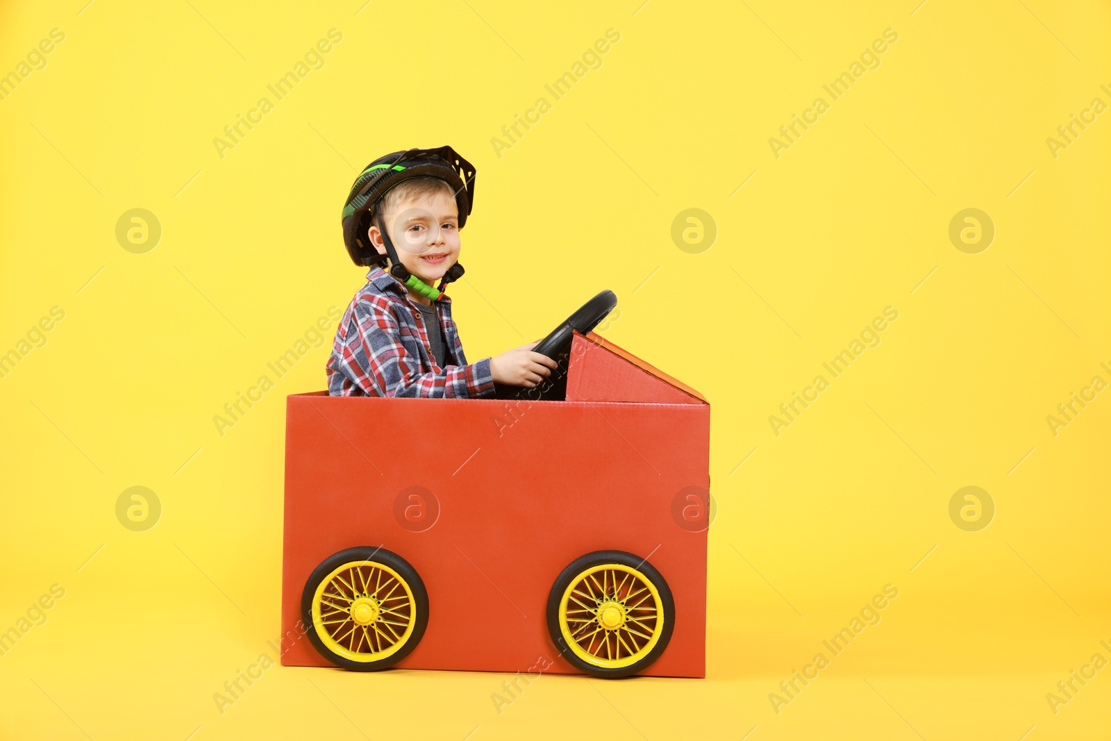 Photo of Little boy driving car made of cardboard on yellow background