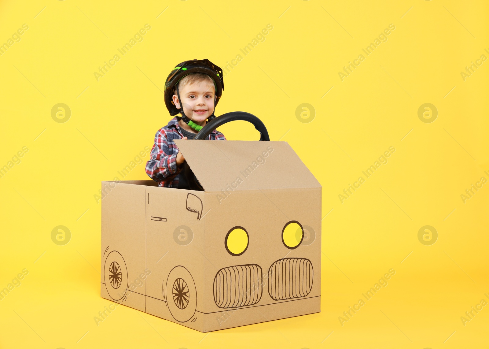 Photo of Little boy driving car made of cardboard on yellow background