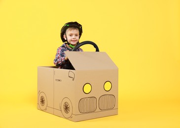 Little boy driving car made of cardboard on yellow background