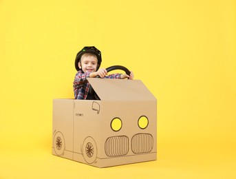 Little boy driving car made of cardboard on yellow background. Space for text