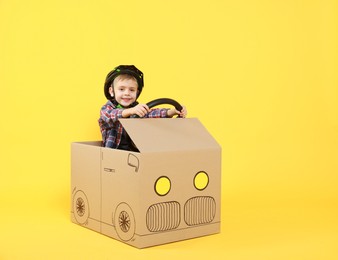 Photo of Little boy driving car made of cardboard on yellow background. Space for text