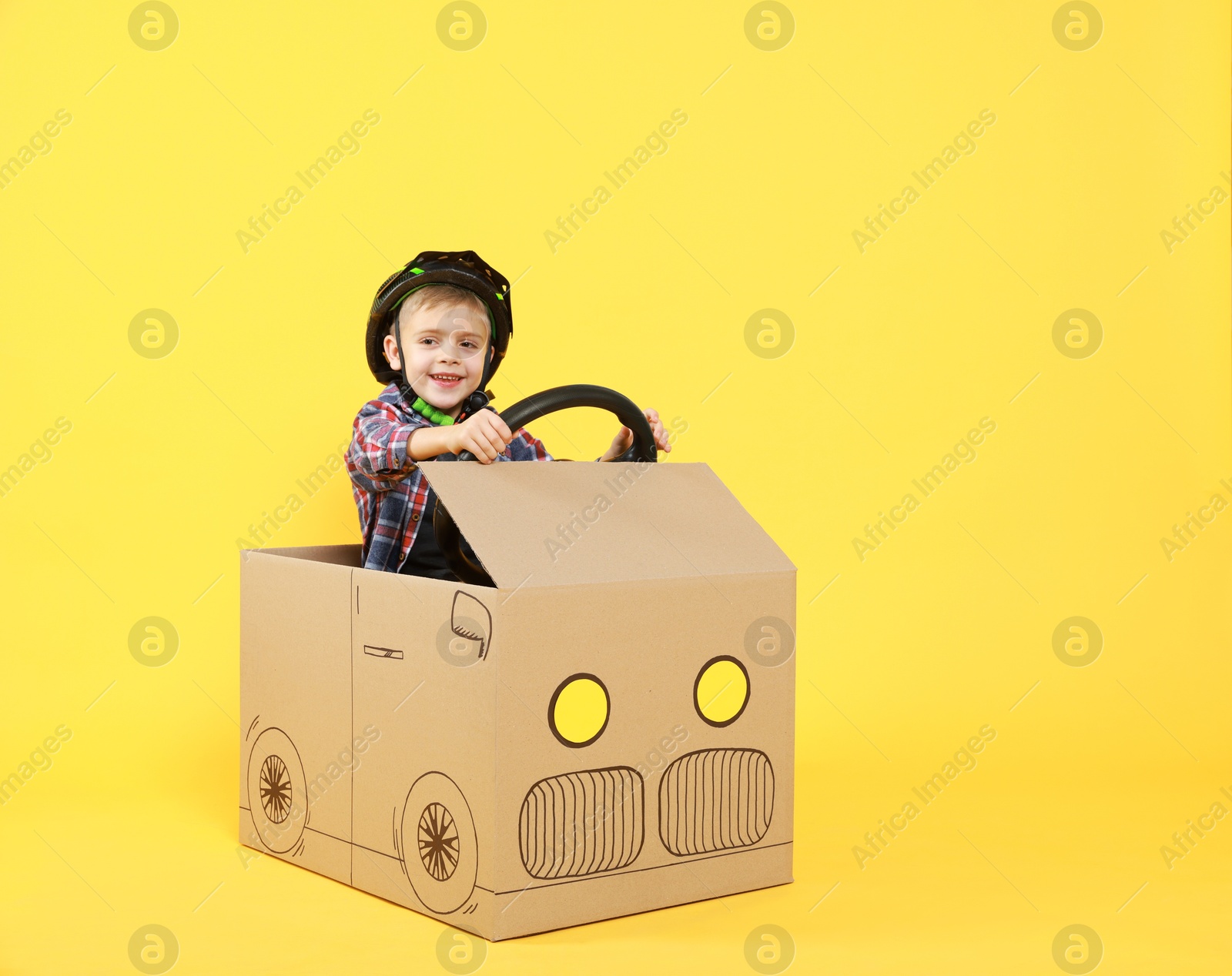 Photo of Little boy driving car made of cardboard on yellow background. Space for text