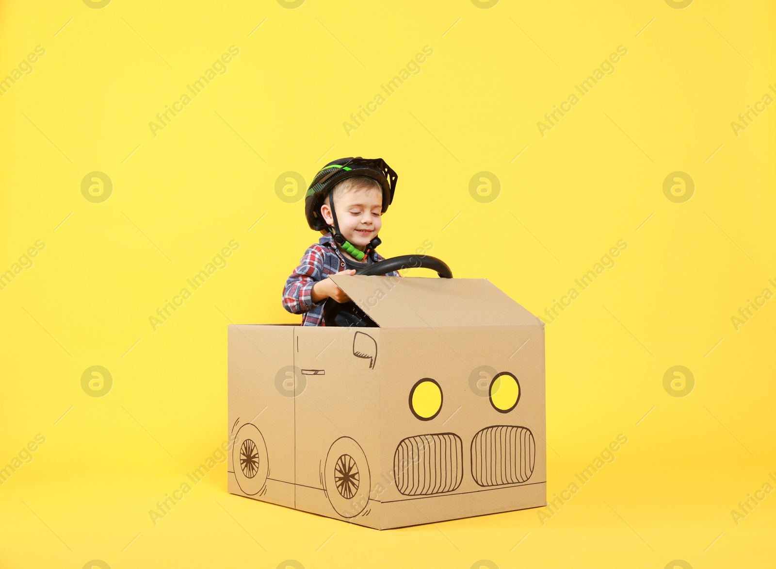 Photo of Little boy driving car made of cardboard on yellow background