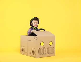 Photo of Little boy driving car made of cardboard on yellow background