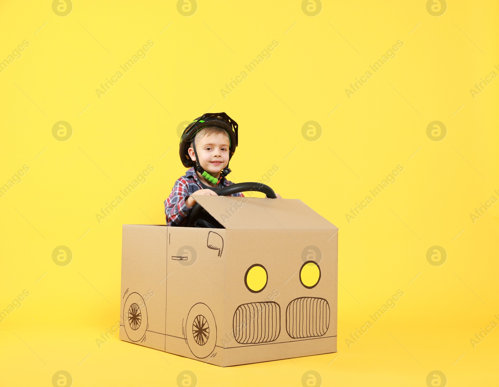 Photo of Little boy driving car made of cardboard on yellow background