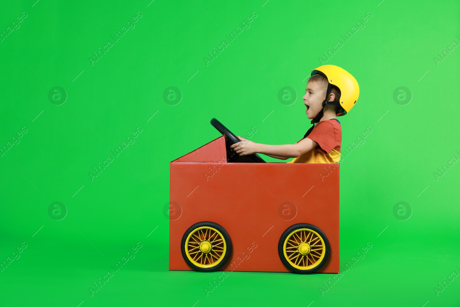 Photo of Little boy driving car made of cardboard on green background