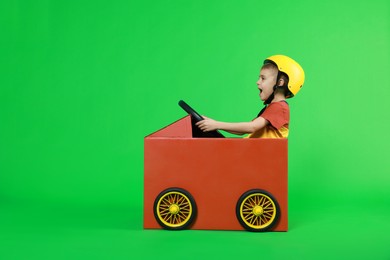 Little boy driving car made of cardboard on green background