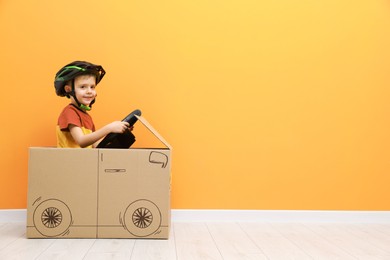 Photo of Little boy driving car made of cardboard against orange wall. Space for text