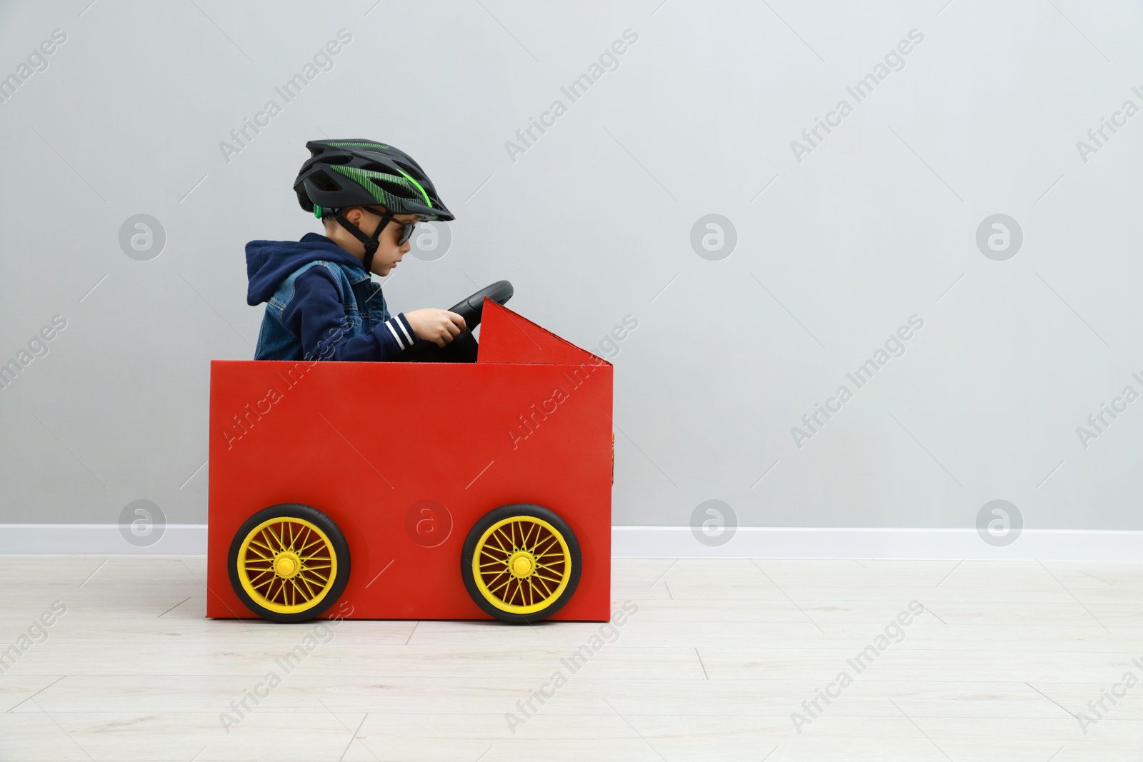 Photo of Little boy driving car made of cardboard against light wall. Space for text