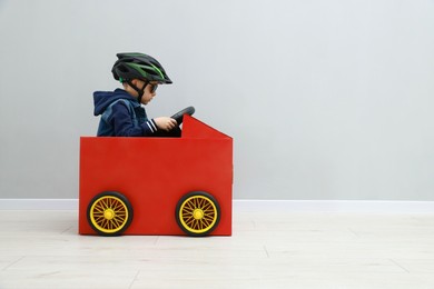 Little boy driving car made of cardboard against light wall. Space for text