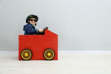 Little boy driving car made of cardboard against light wall. Space for text