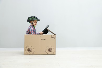 Little boy driving car made of cardboard against light wall. Space for text