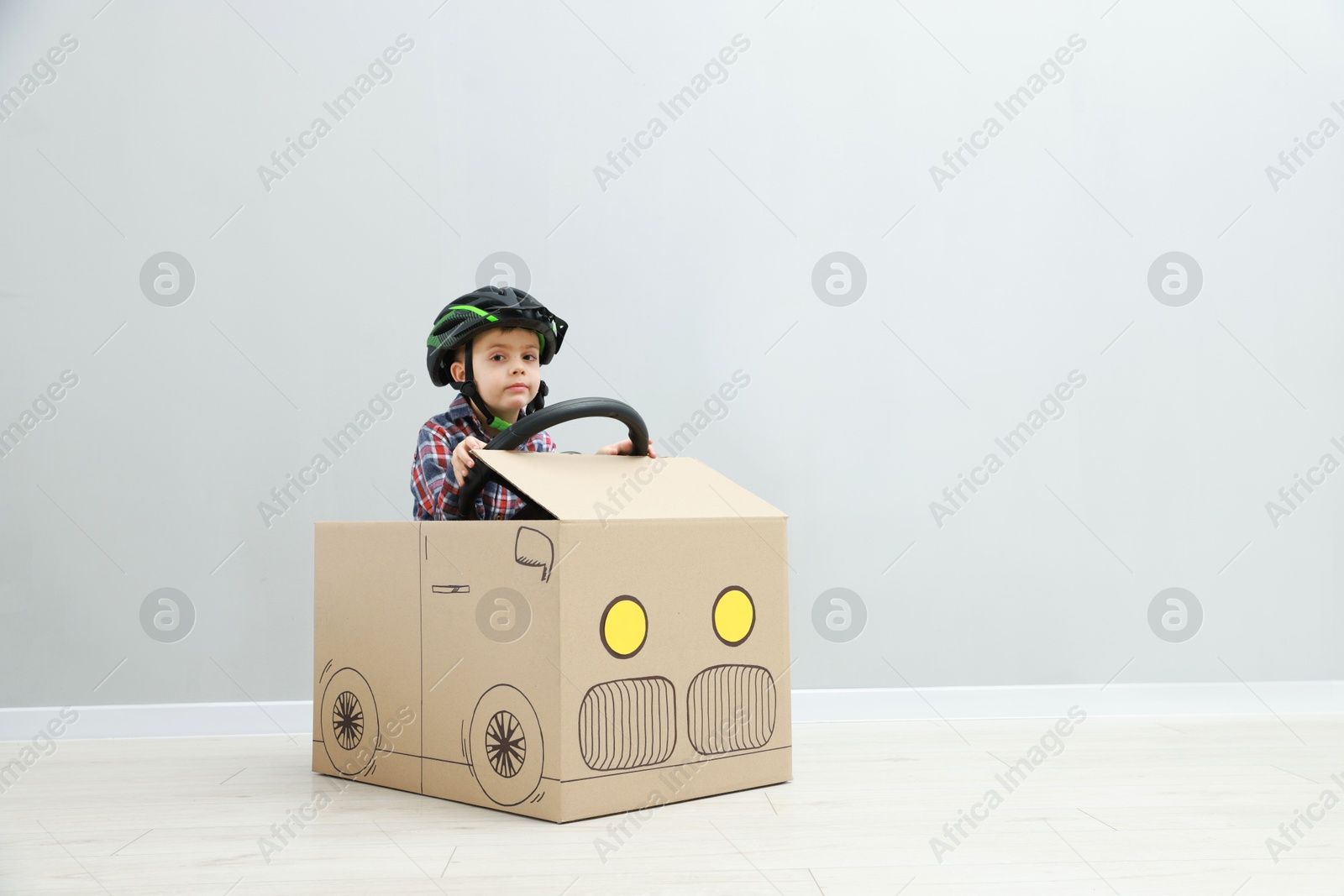 Photo of Little boy driving car made of cardboard against light wall. Space for text