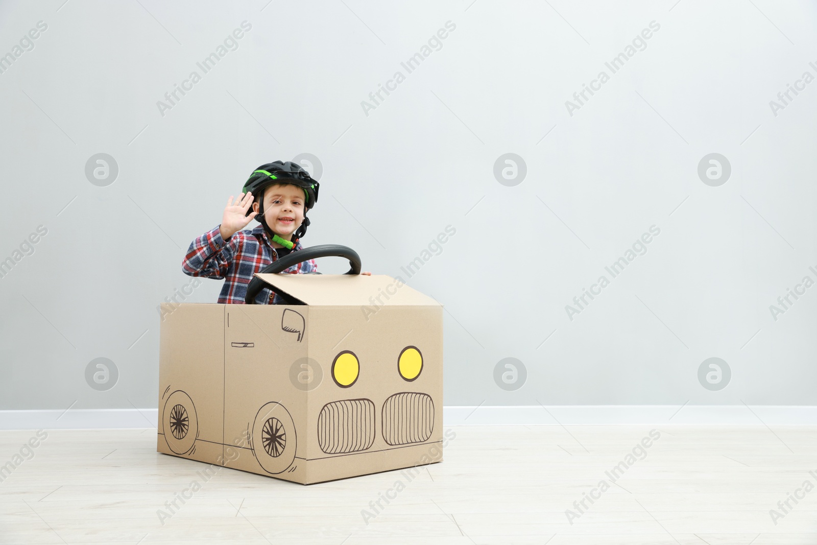 Photo of Little boy driving car made of cardboard against light wall. Space for text