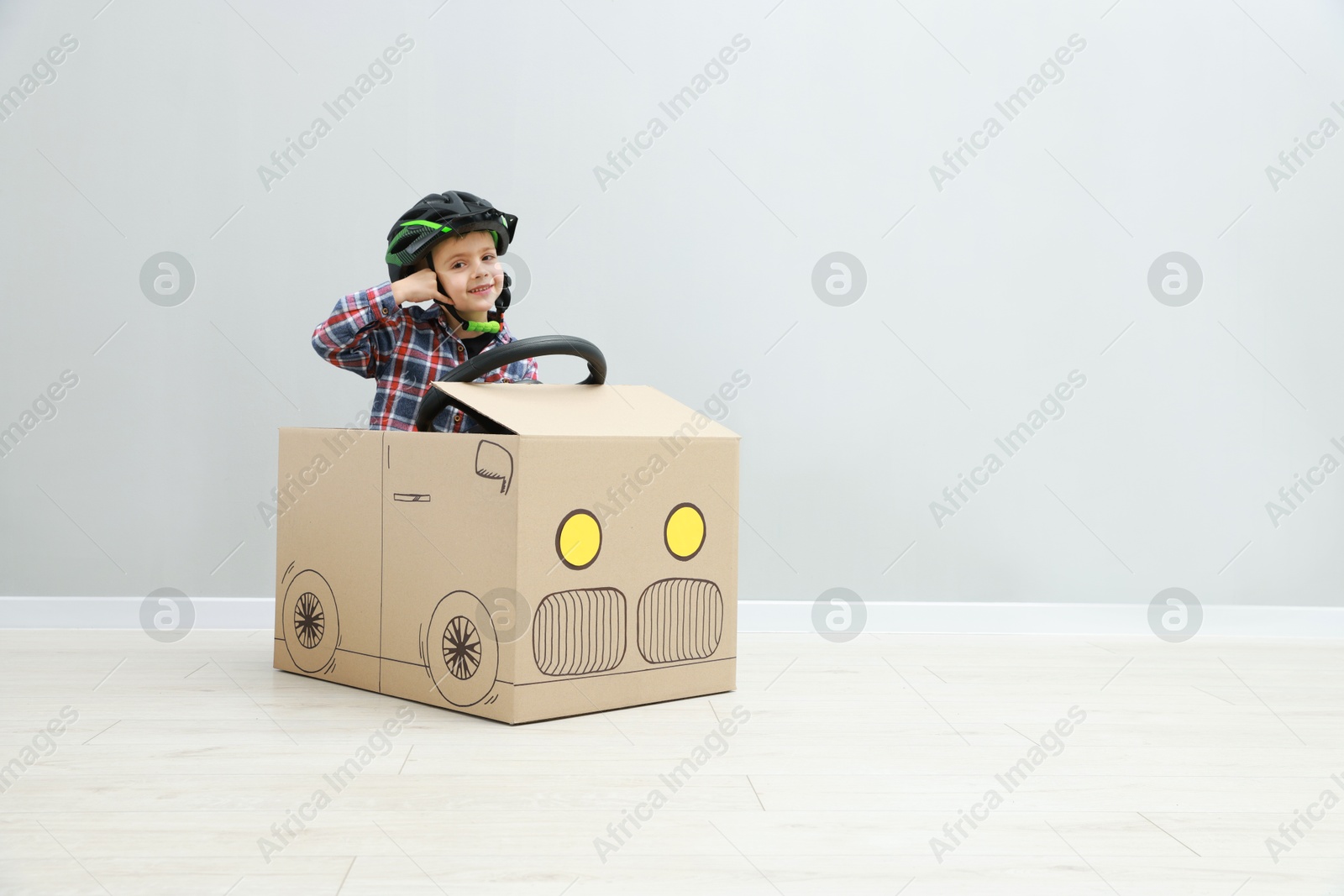 Photo of Little boy driving car made of cardboard against light wall. Space for text