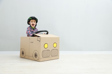 Little boy driving car made of cardboard against light wall. Space for text