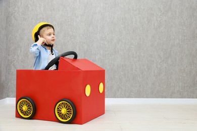 Little boy driving car made of cardboard against grey wall. Space for text