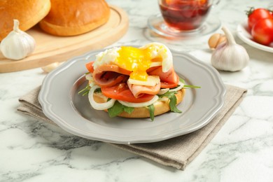 Photo of Tasty brunch. Poached egg, ham, tomato, arugula and bun on white marble table, closeup