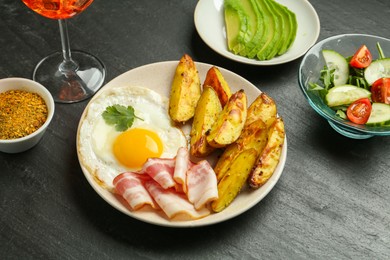 Photo of Tasty brunch. Fried egg, potato, bacon and salad on dark textured table, closeup