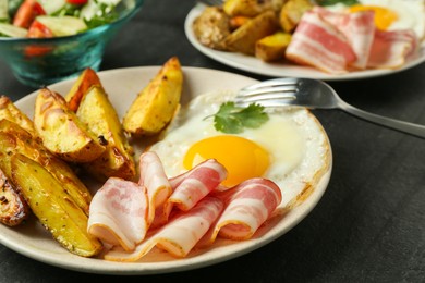 Photo of Tasty brunch. Fried egg, potato, bacon and fork on dark textured table, closeup