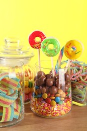 Candy bar. Many different sweets on wooden table against yellow background, closeup